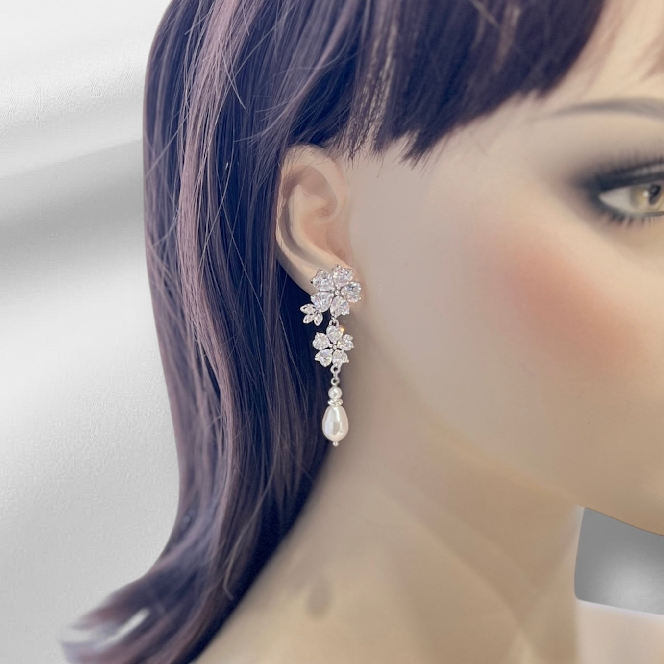 Close-up of a woman wearing a floral earring with a pearl drop on a neutral background