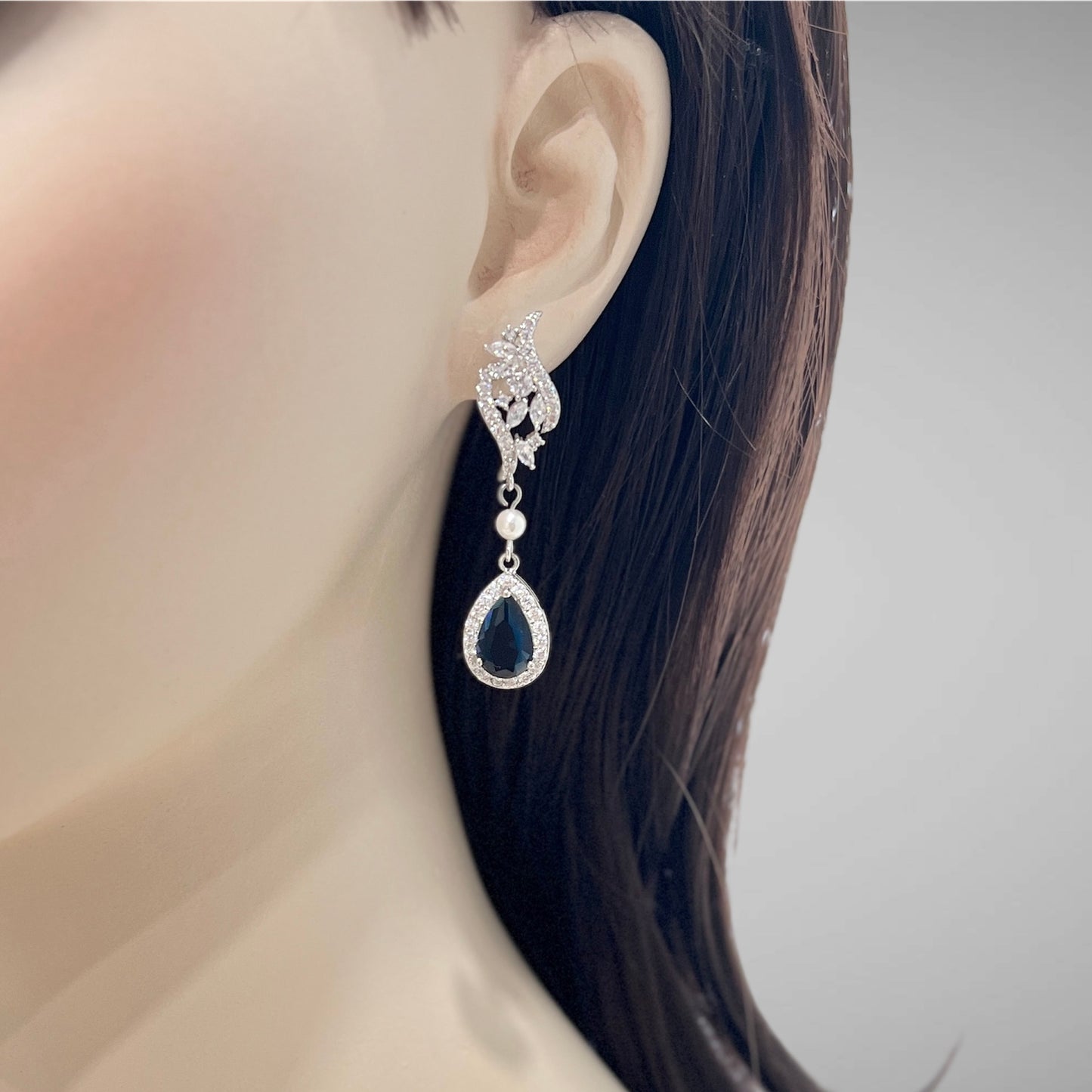 Earring with a blue teardrop gemstone worn by a person with dark hair.