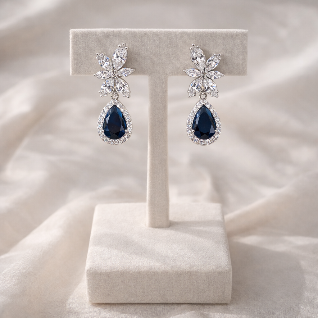 Pair of earrings with blue teardrop stones on a white stand against a soft white background