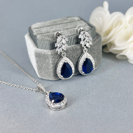 Jewelry set with sapphire blue teardrop stones on a gray surface.