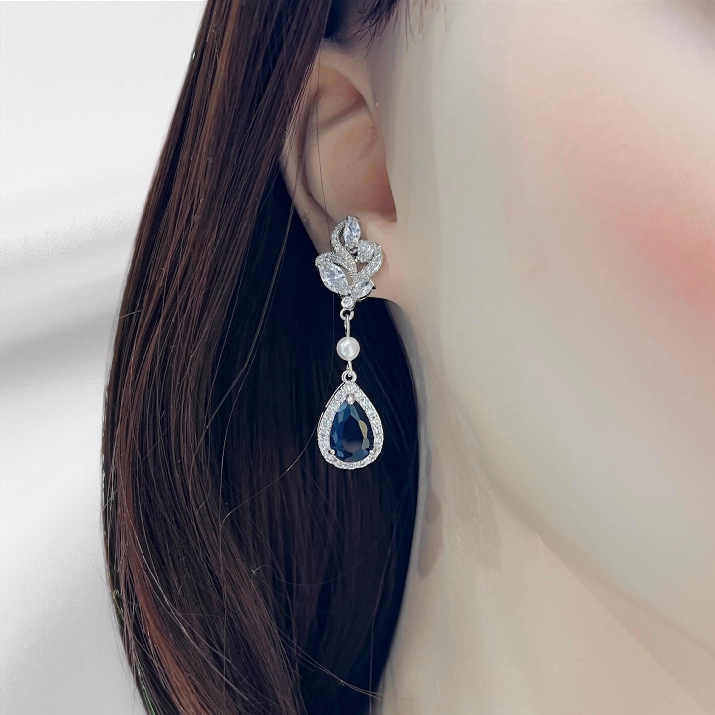 Teardrop sapphire crystal earrings with pearl accent photographed on earlobe