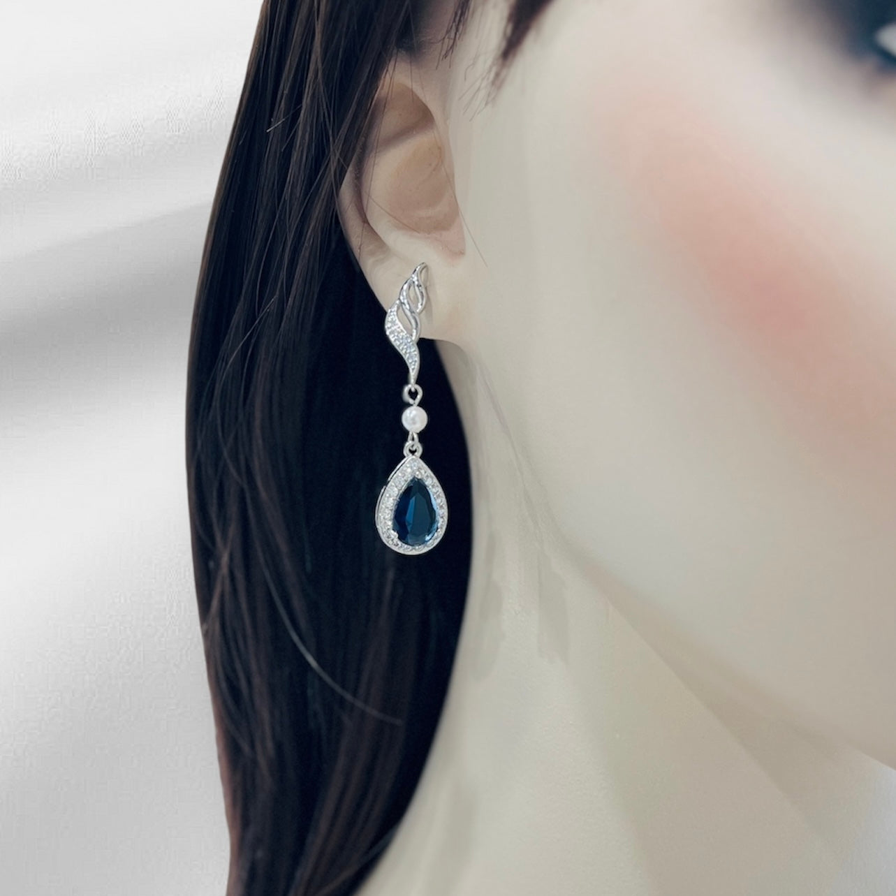 Earring with a blue gemstone worn by a person with dark hair.