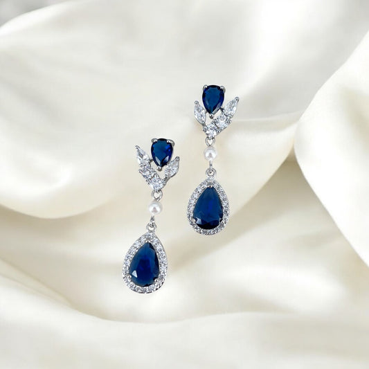 Pair of blue teardrop earrings with silver and pearl accents on a white fabric background