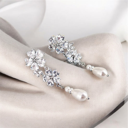 Silver earrings with crystal and pearl details on a white surface