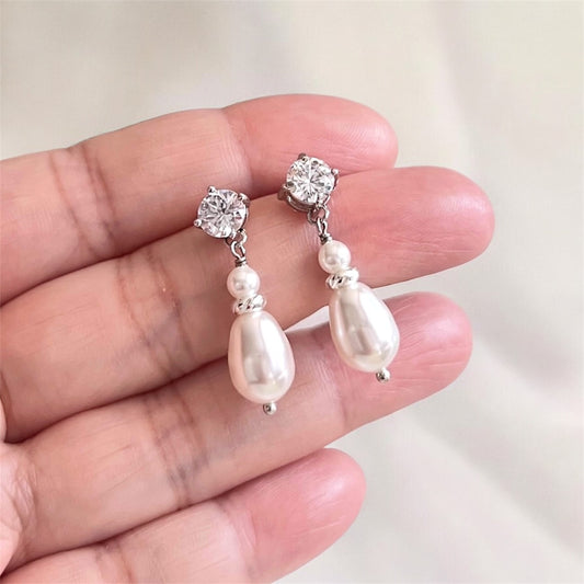 Pearl and crystal drop earrings held between fingers against a neutral background