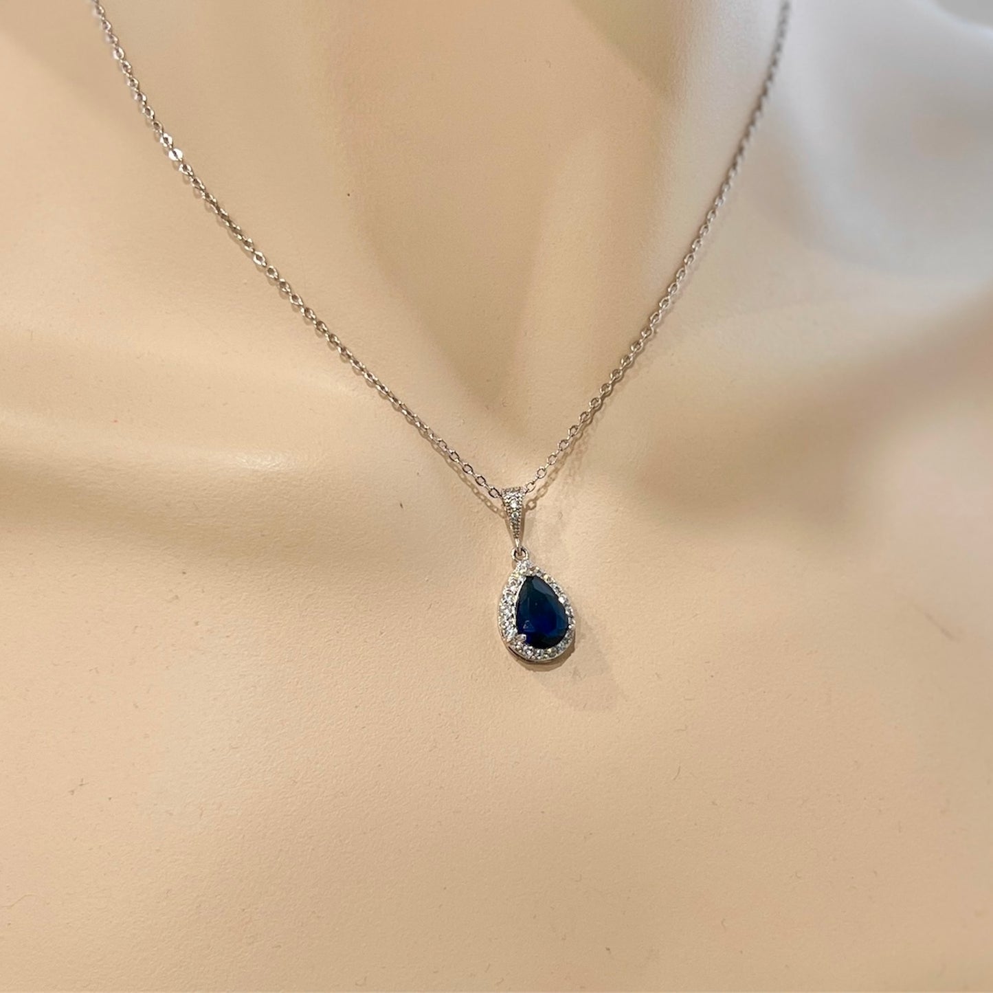 Silver necklace with a blue teardrop pendant on a mannequin.