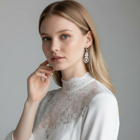 Woman wearing a white lace top and earrings against a gray background