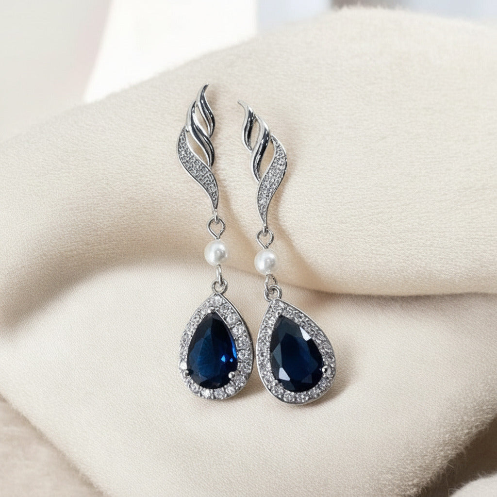 Pair of blue teardrop earrings with silver and pearl accents on a soft pink fabric background.