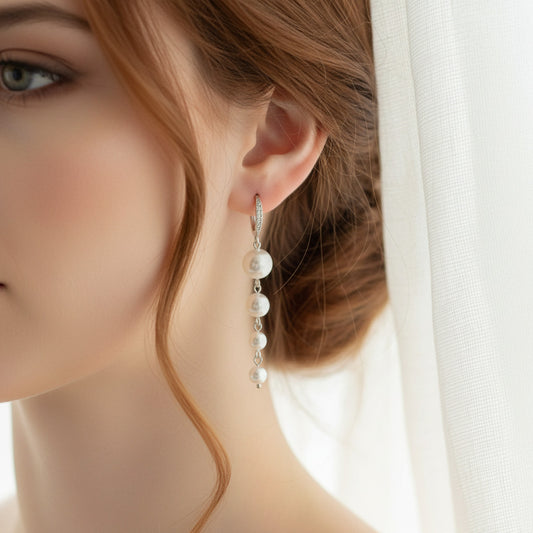 Long white pearl dangle earrings silver bridal jewelry on a model's earlobe