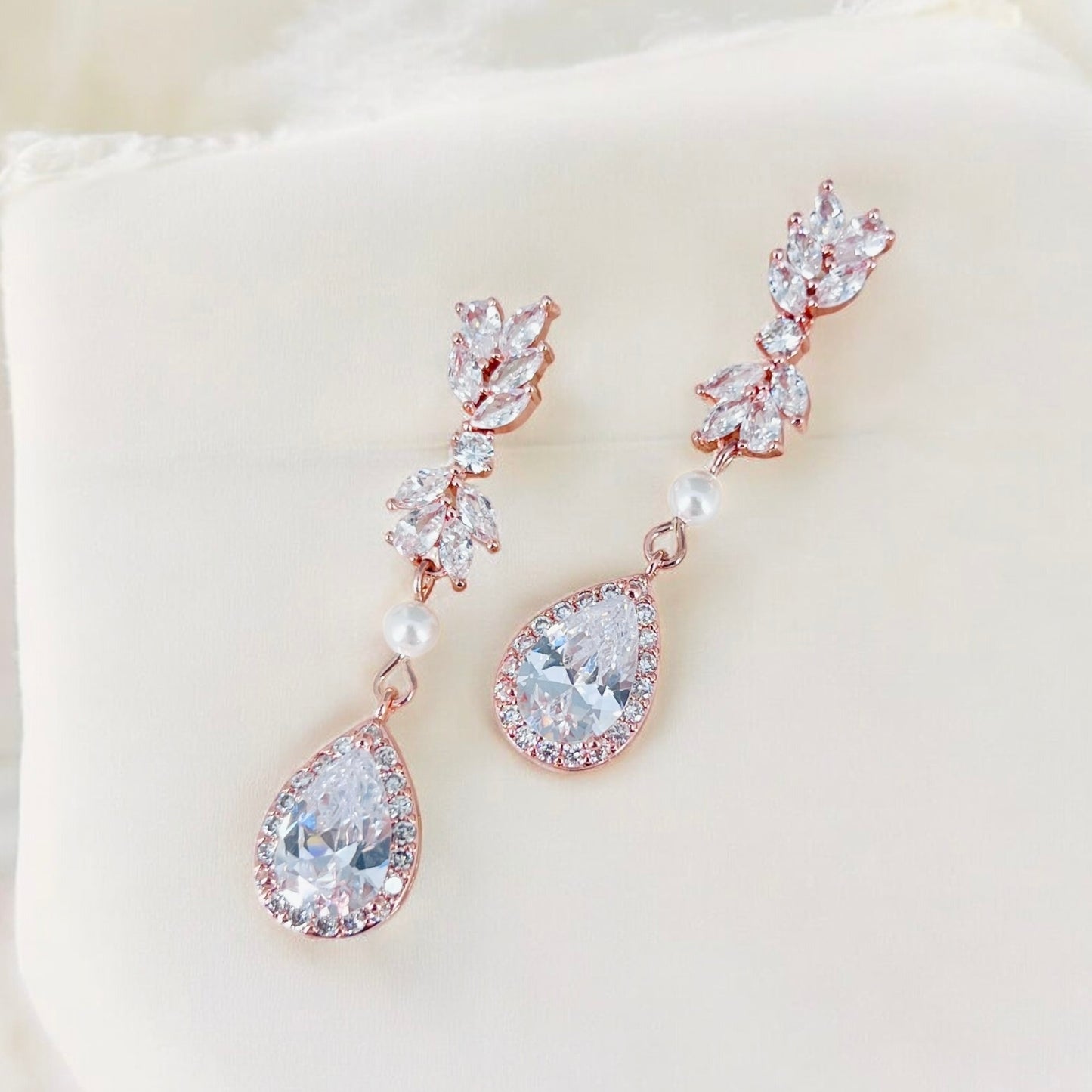 Handmade rose gold bridal earrings with clear stones shown against neutral fabric for product clarity