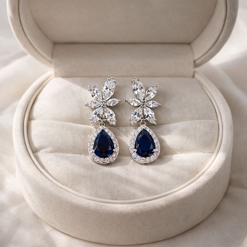 Pair of blue teardrop earrings with silver accents on a beige jewelry box.