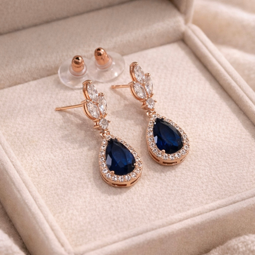 Rose gold earrings with blue teardrop stones on a beige jewelry box