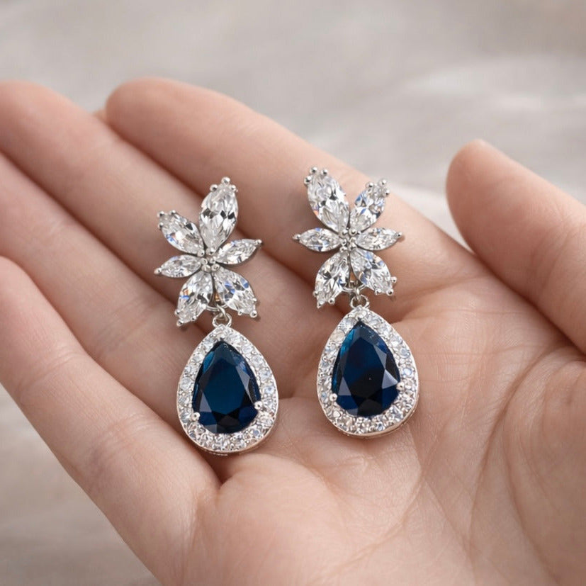 Pair of blue gemstone earrings held in a hand with a blurred background