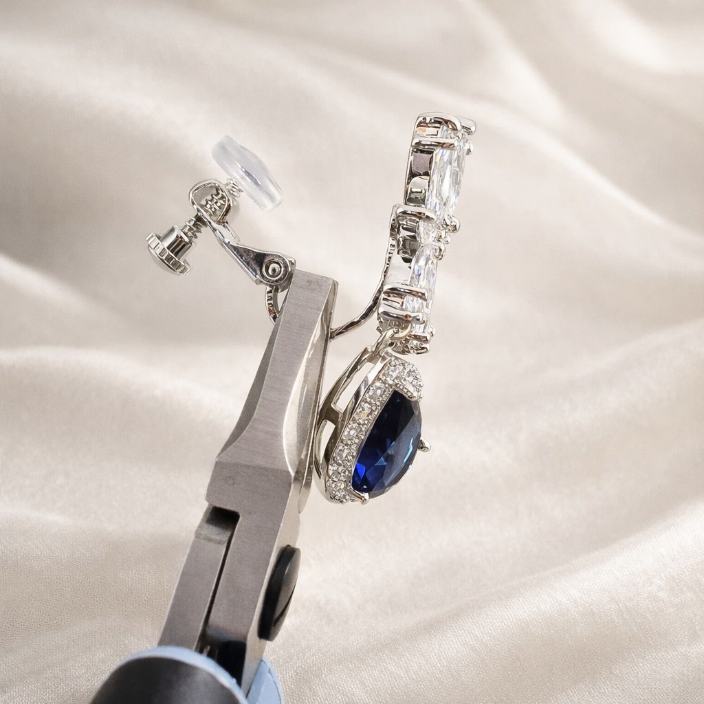 Pair of earrings with a blue gemstone held by pliers on a satin background