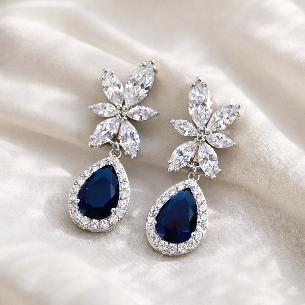 Pair of earrings with blue teardrop stones and floral designs on a white fabric background