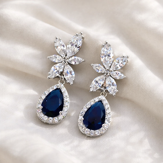 Pair of earrings with blue teardrop stones and floral designs on a white fabric background