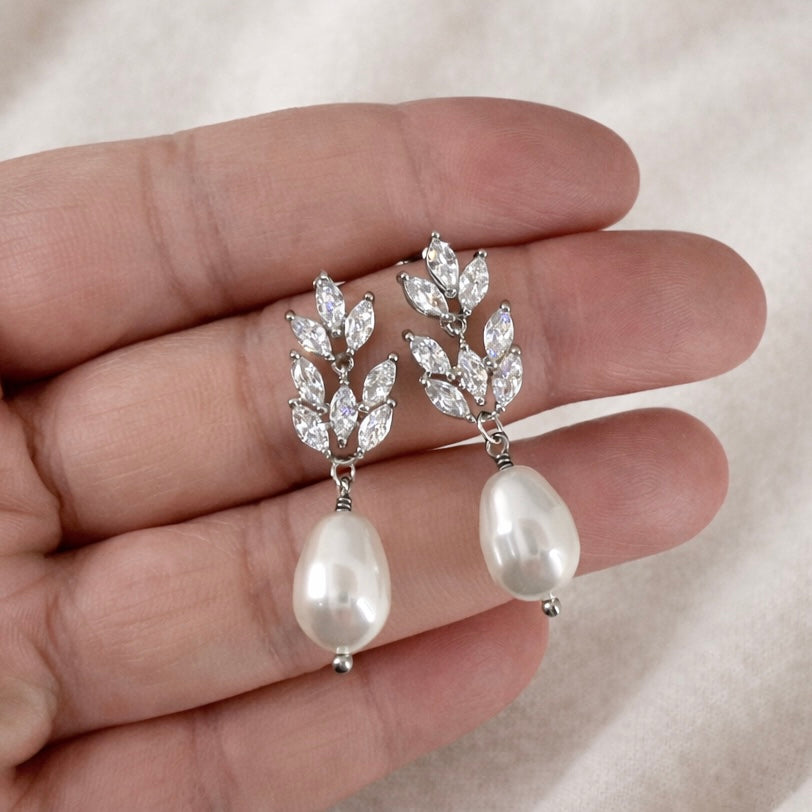 Pearl and crystal earrings held in a hand against a neutral background