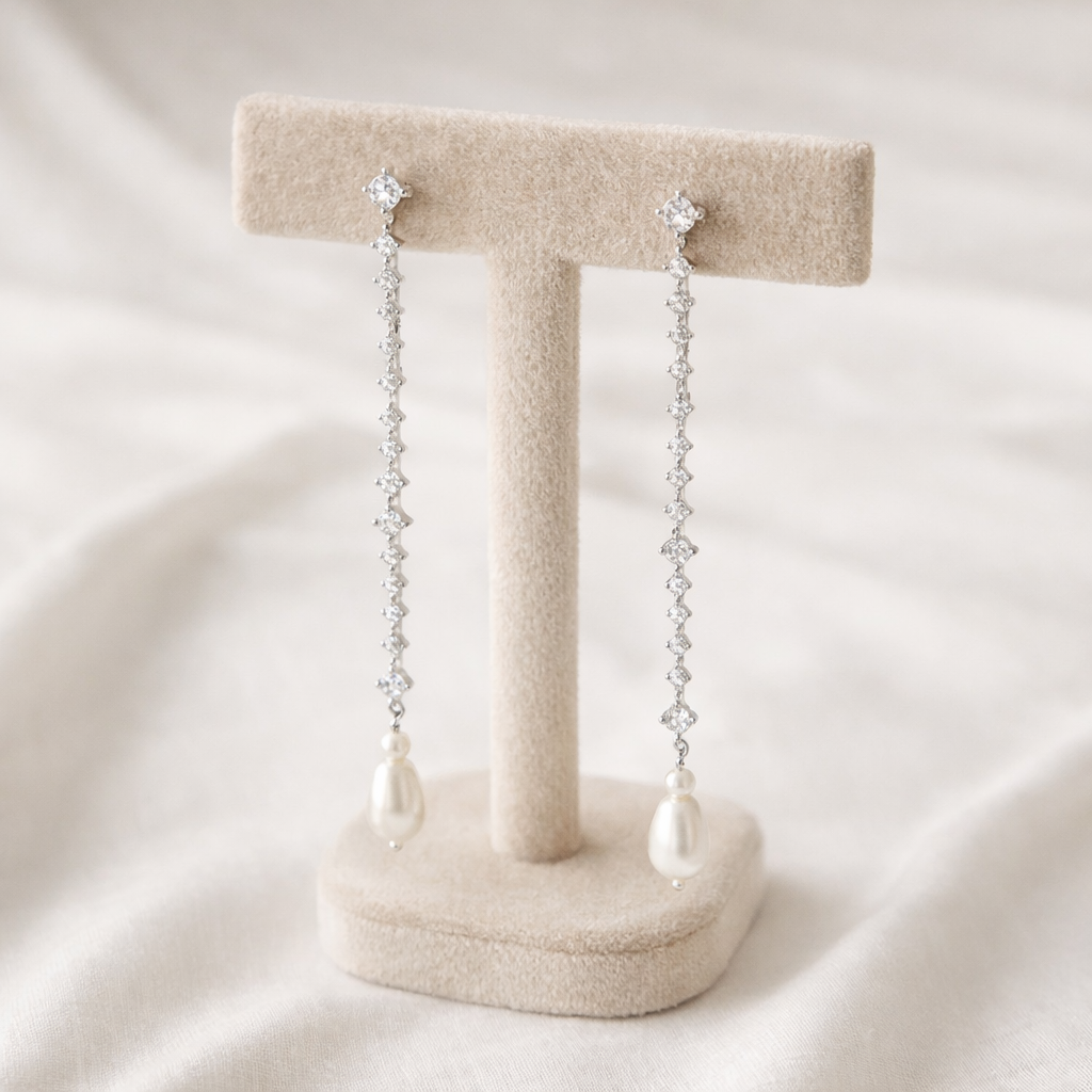 Pair of pearl and crystal drop earrings on a beige stand against a white background