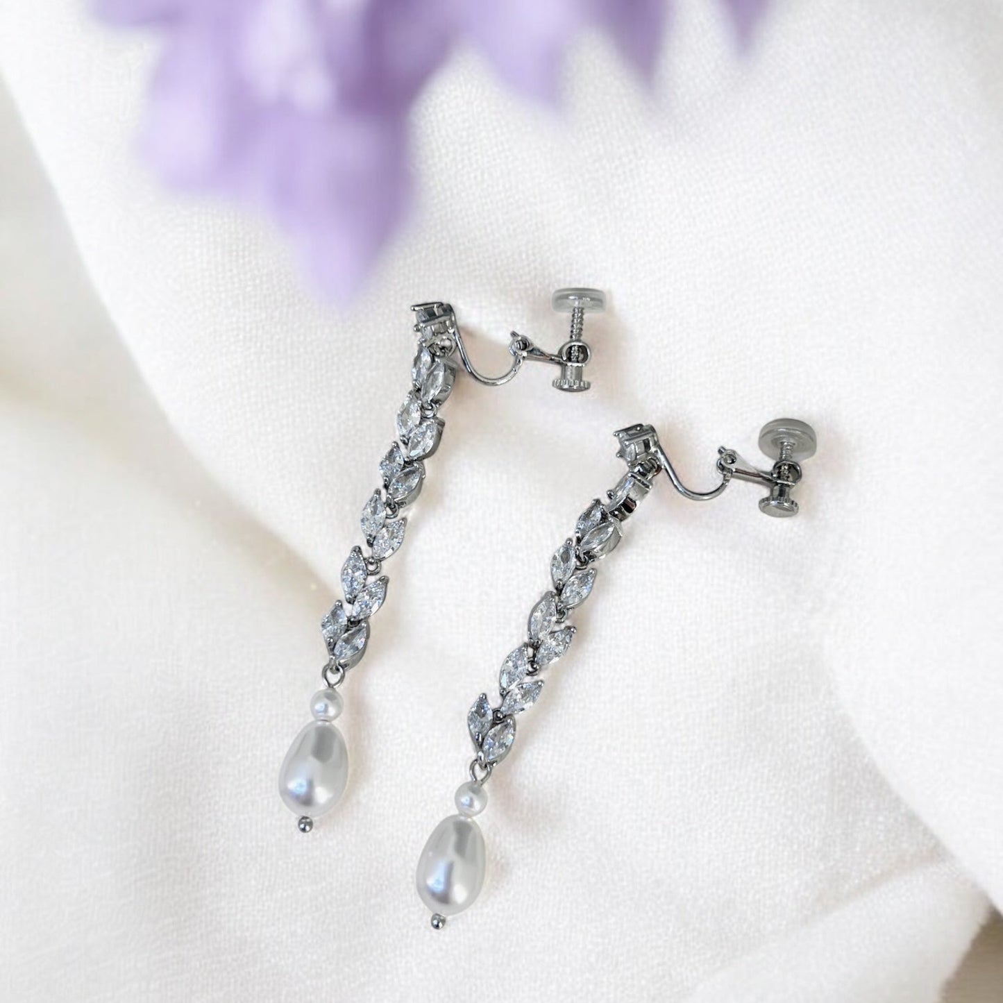 Silver lip on earrings with pear-shaped pearl drops on a white surface 