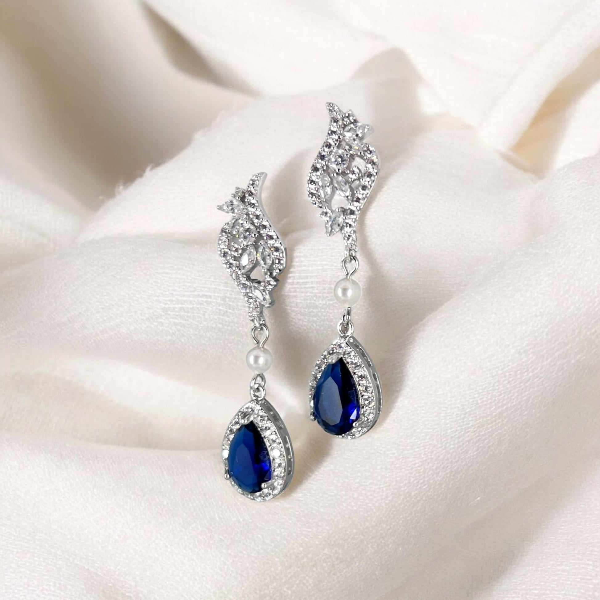 Pair of silver earrings with teardrop blue gemstones on a white fabric background