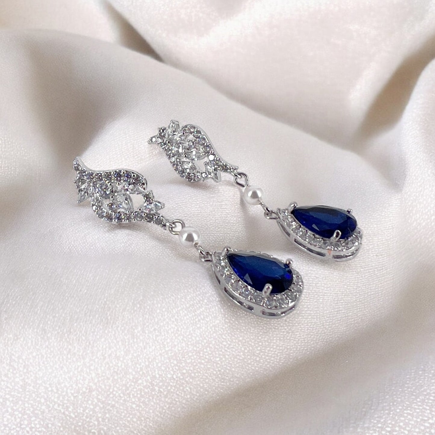 Pair of silver earrings with blue teardrop gemstones on a white fabric background