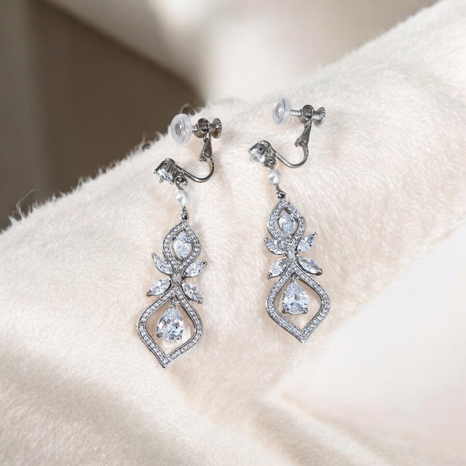 Pair of silver earrings with clear gemstones on a soft fabric background
