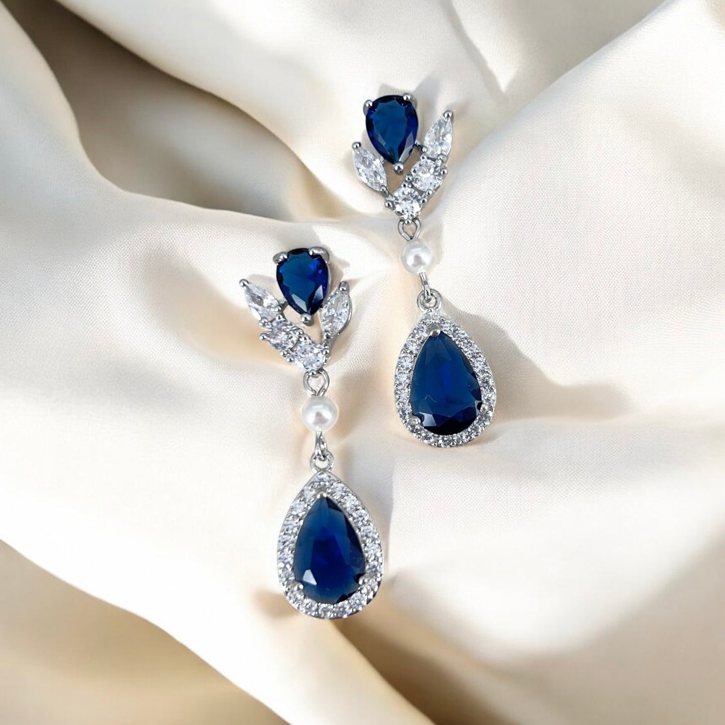 Pair of blue teardrop earrings with pearl accents on a beige fabric background