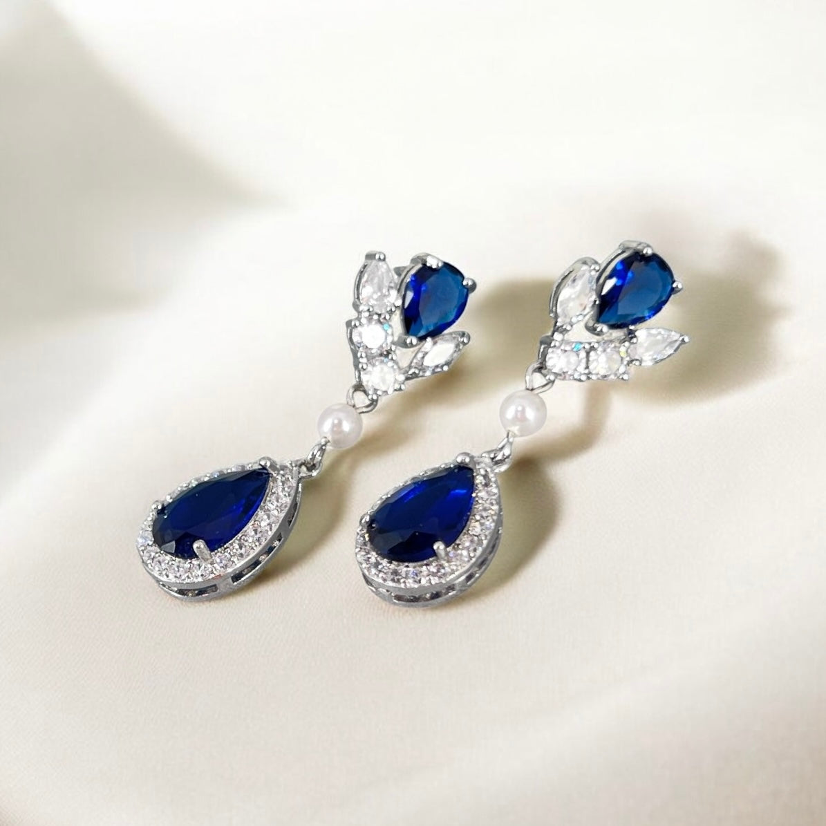 Pair of blue teardrop earrings with pearl accents on a white background