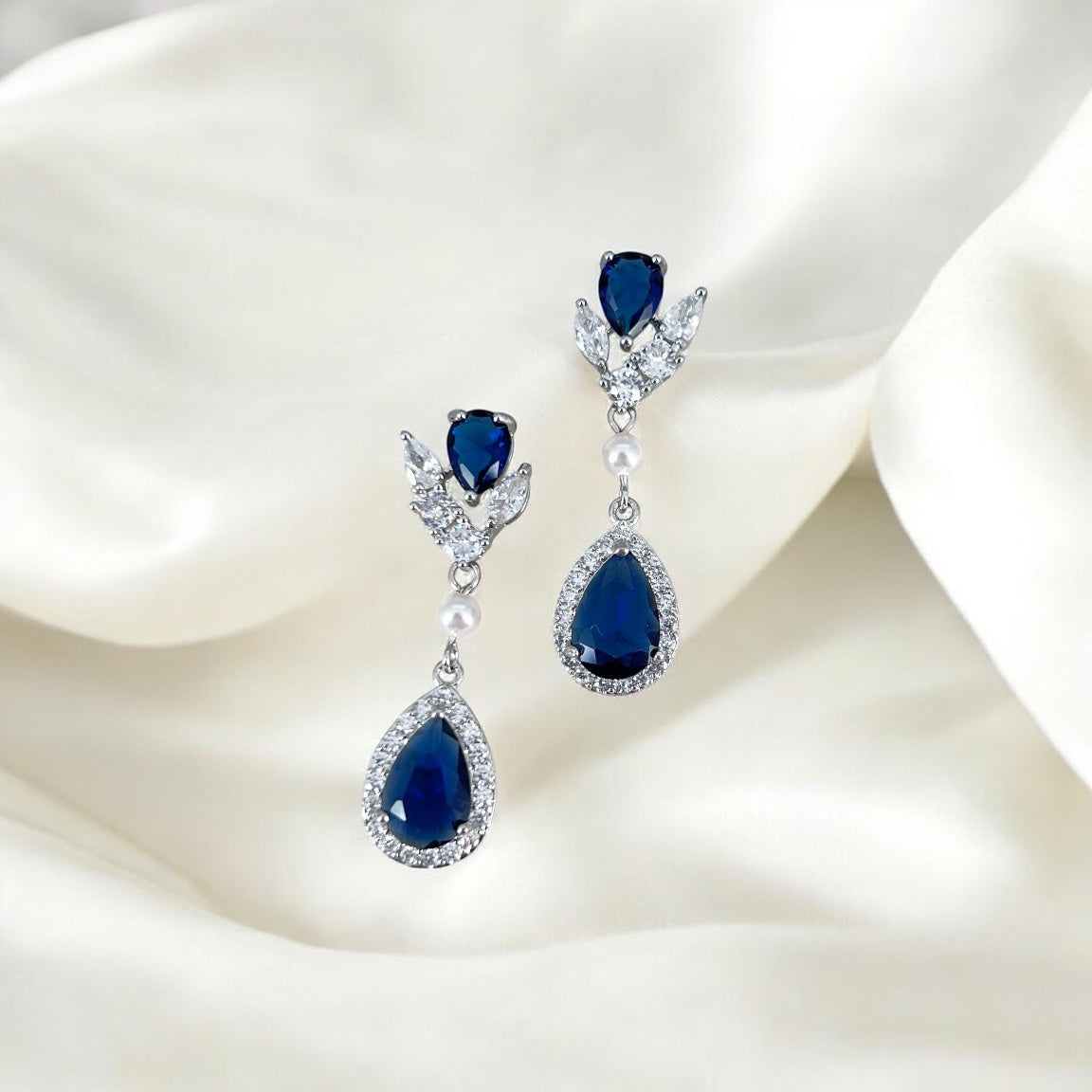 Pair of blue teardrop earrings with silver and pearl accents on a white fabric background