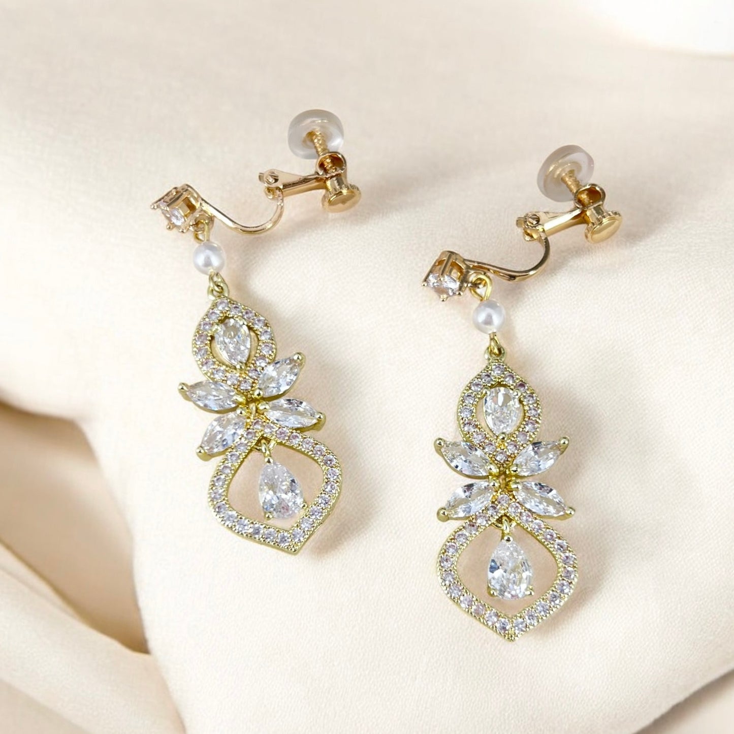 Gold earrings with clear stones and pearls on a beige fabric background