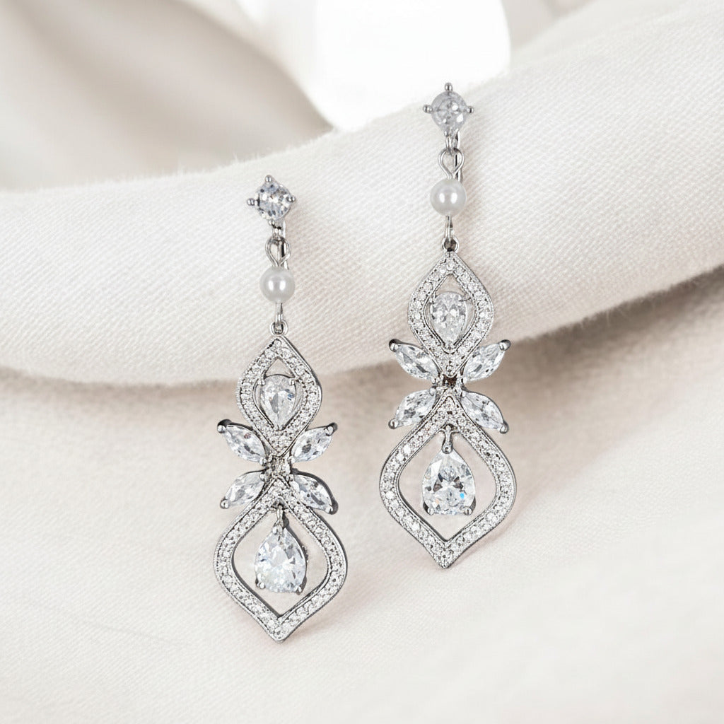 Pair of silver earrings with clear gemstones and pearls on a white background