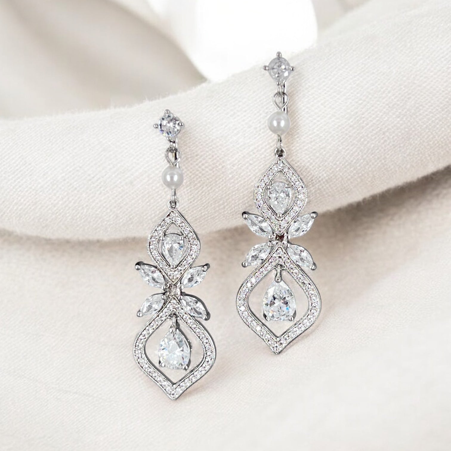 Pair of silver earrings with clear gemstones and pearls on a white background