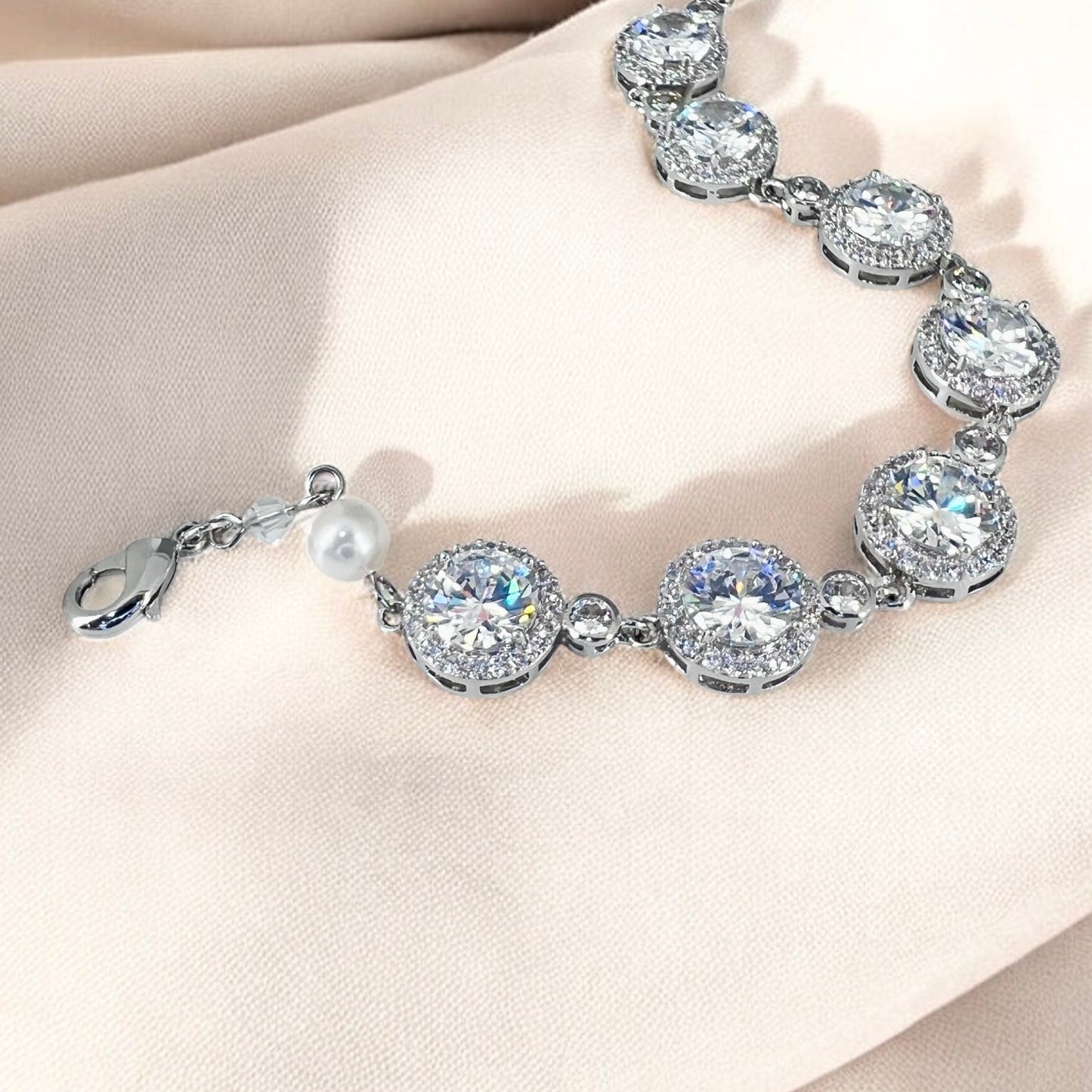 Sparkling bridal crystal tennis bracelet with round clear stones and pearl accents displayed on soft fabric