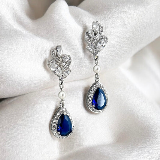 Sapphire blue teardrop bridal earrings with crystal halo photographed on soft neutral fabric