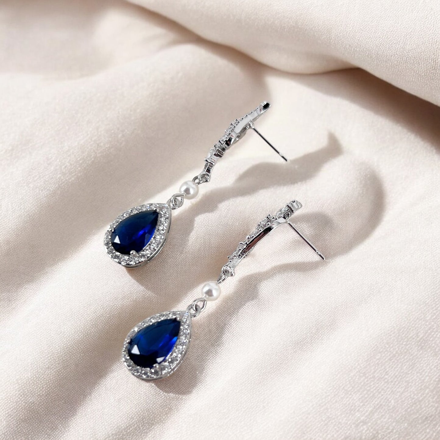 A pair of blue teardrop earrings on a light beige fabric background