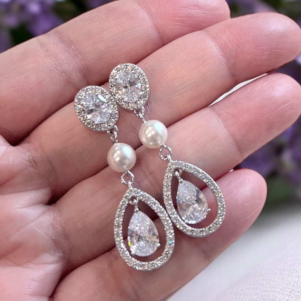 Pearl teardrop crystal bridal earrings with halo stones photographed in hand