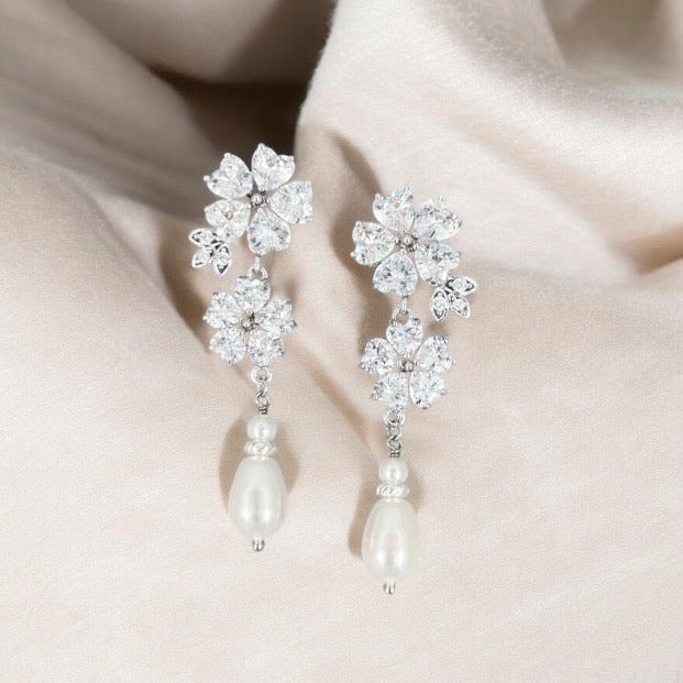 Pair of floral earrings with pearl drops on a soft fabric background