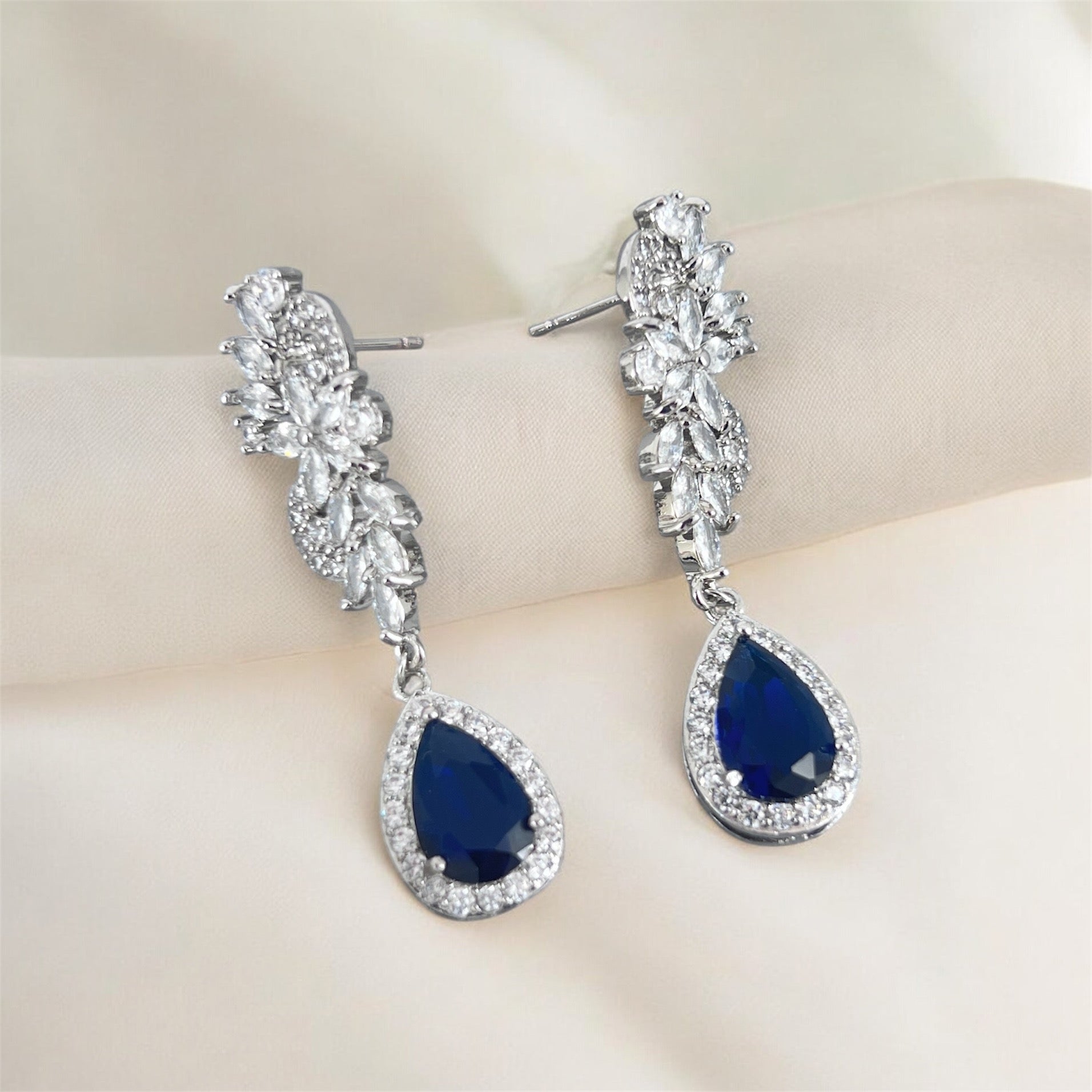 Pair of blue teardrop earrings with silver accents on a off white background