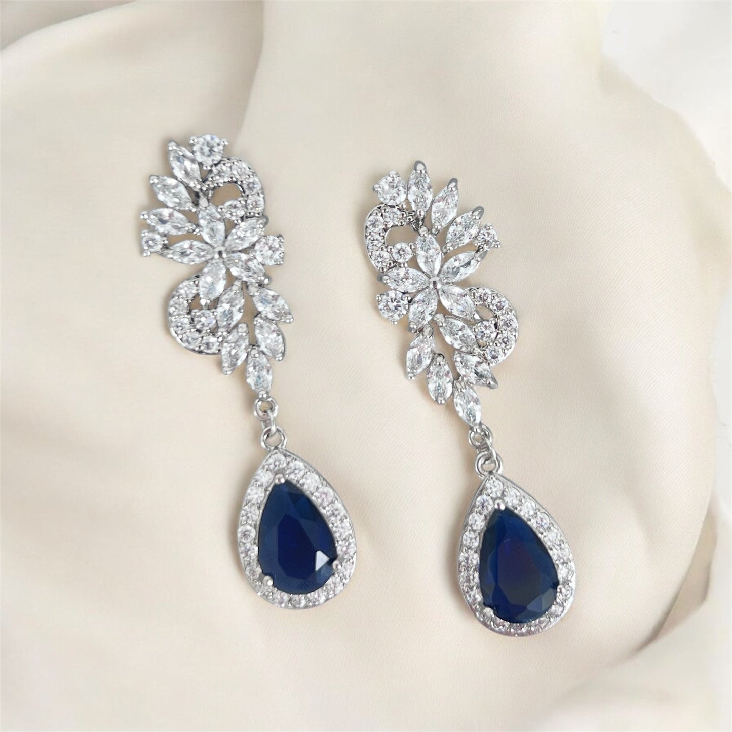 Pair of blue teardrop earrings with silver floral designs on a off white background.