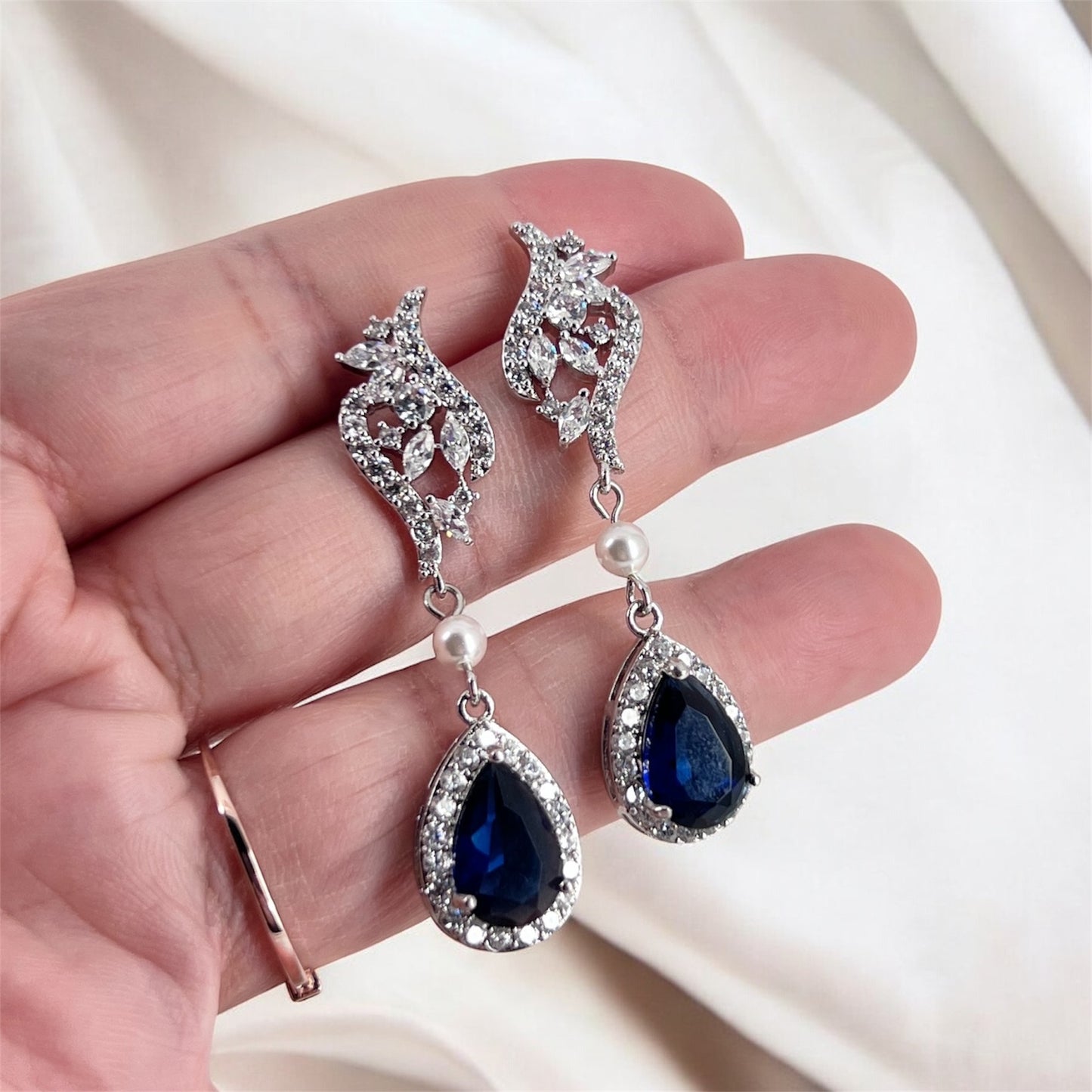 Silver earrings with blue teardrop gemstones held in a hand against a white background