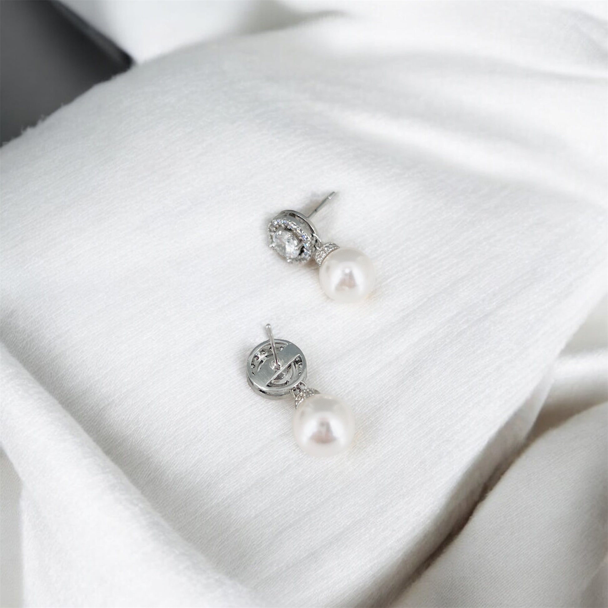 Pearl earrings on a white satin surface