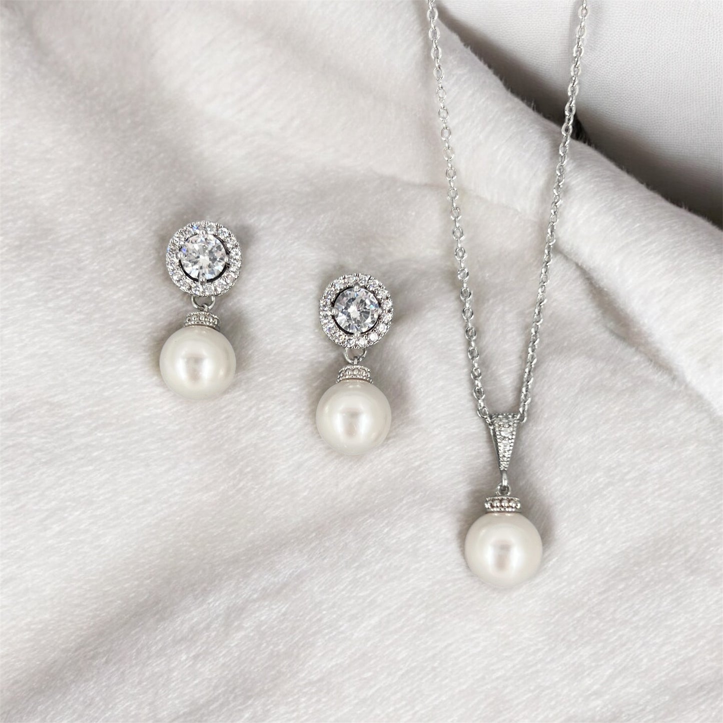 Pearl necklace and earrings set on a white fabric background