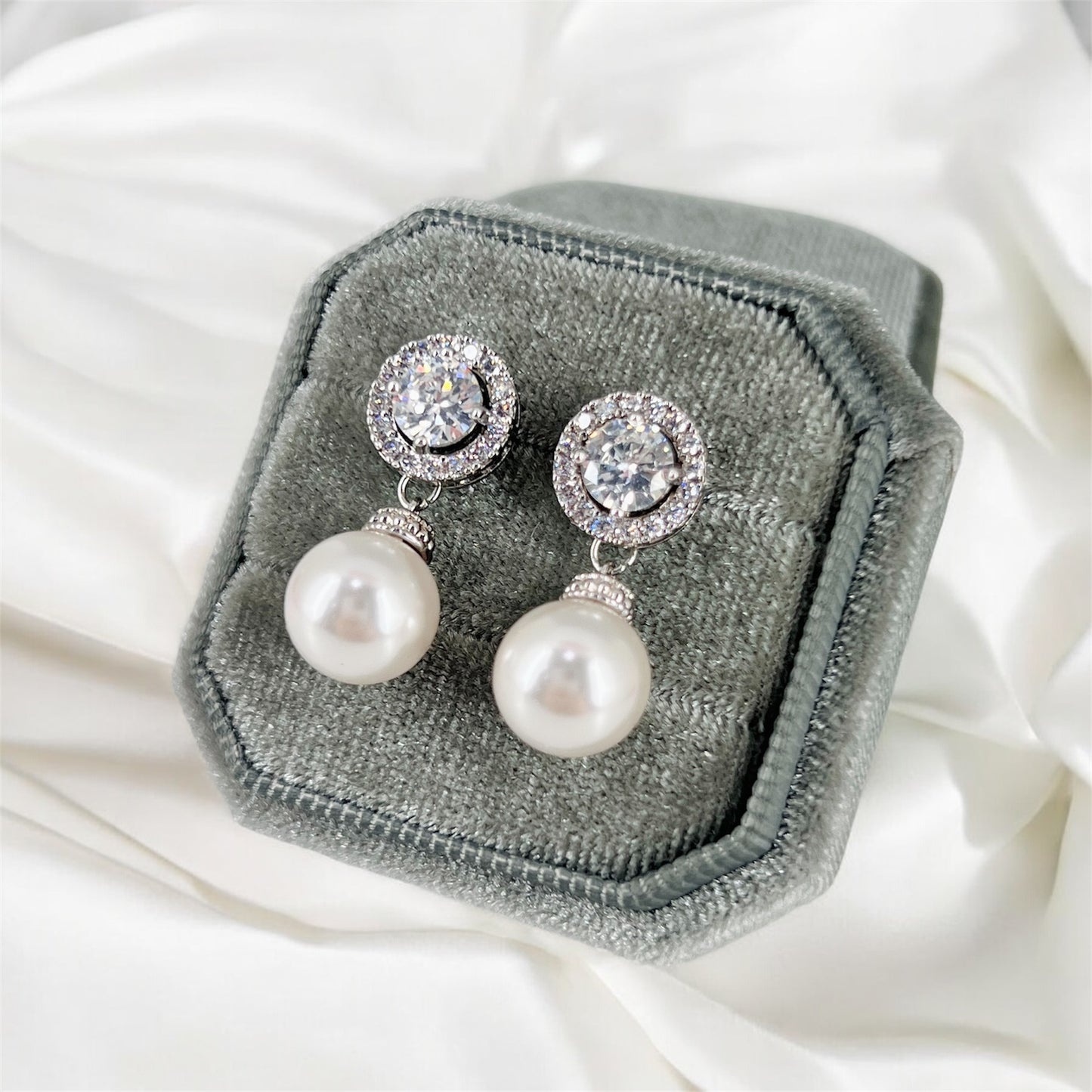 Pearl earrings with silver clasps on a gray velvet cushion