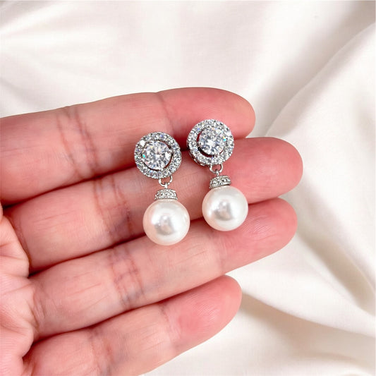 Pearl and crystal drop earrings held in a hand against a soft white background