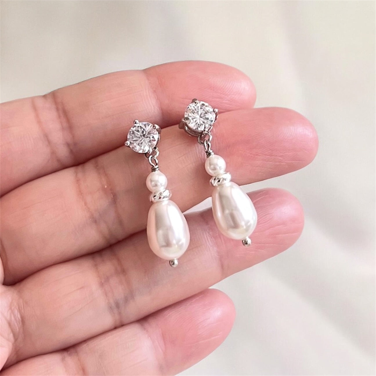 Pearl and crystal drop earrings held between fingers against a neutral background