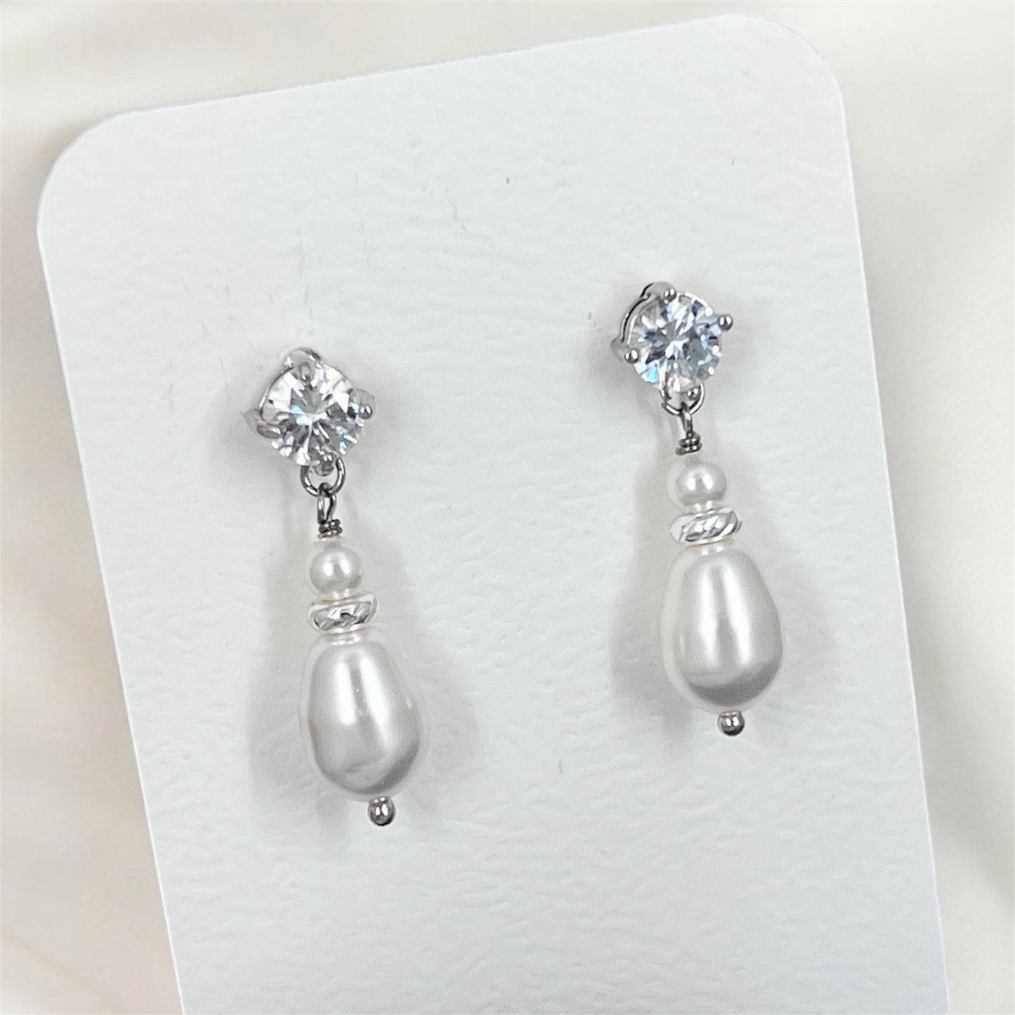 Pair of pearl and crystal drop earrings on a white card