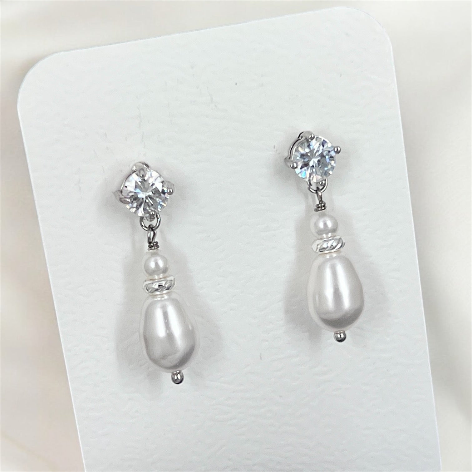 Pair of pearl and crystal drop earrings on a white card