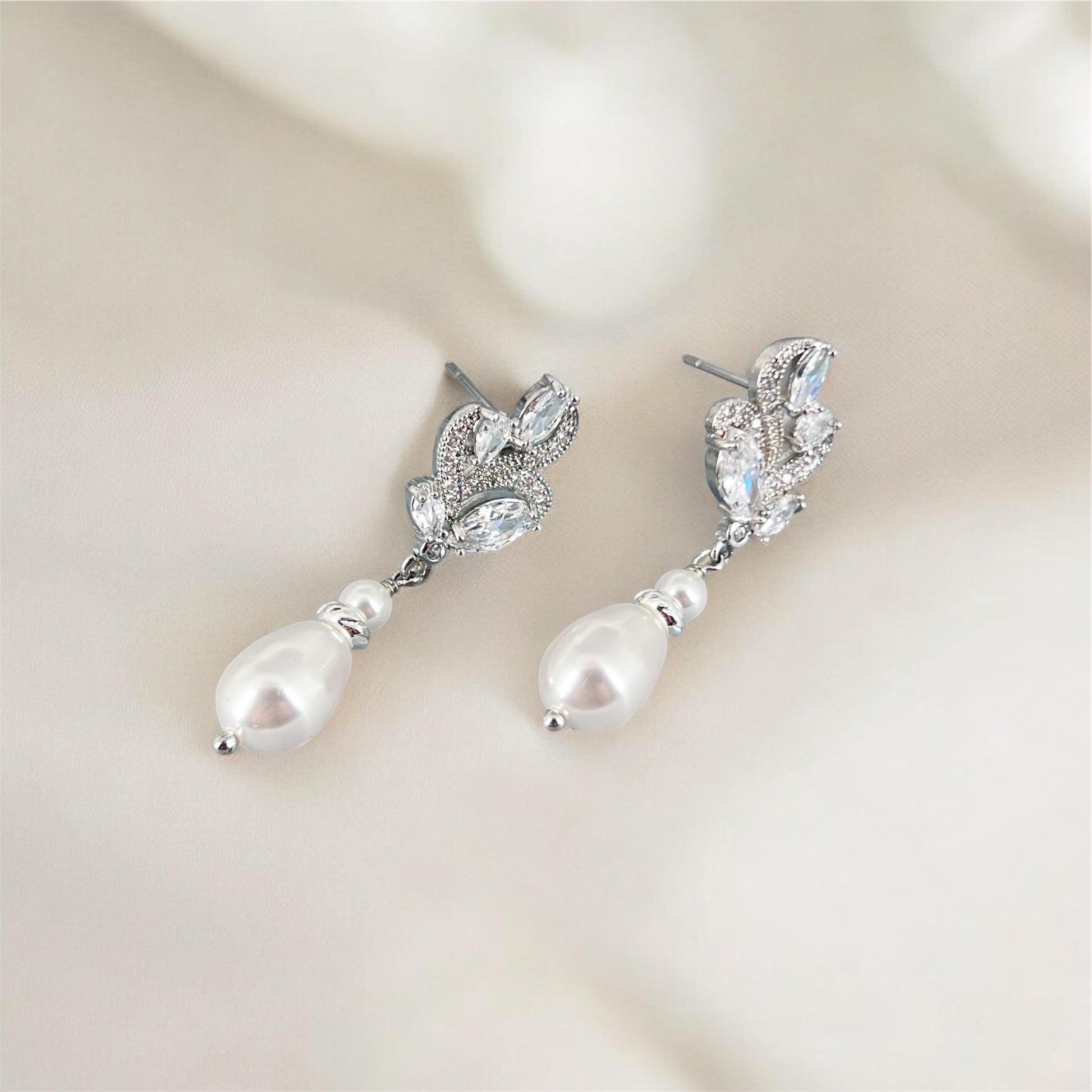 Pair of silver floral marquise earrings with pearl drops on a soft beige background