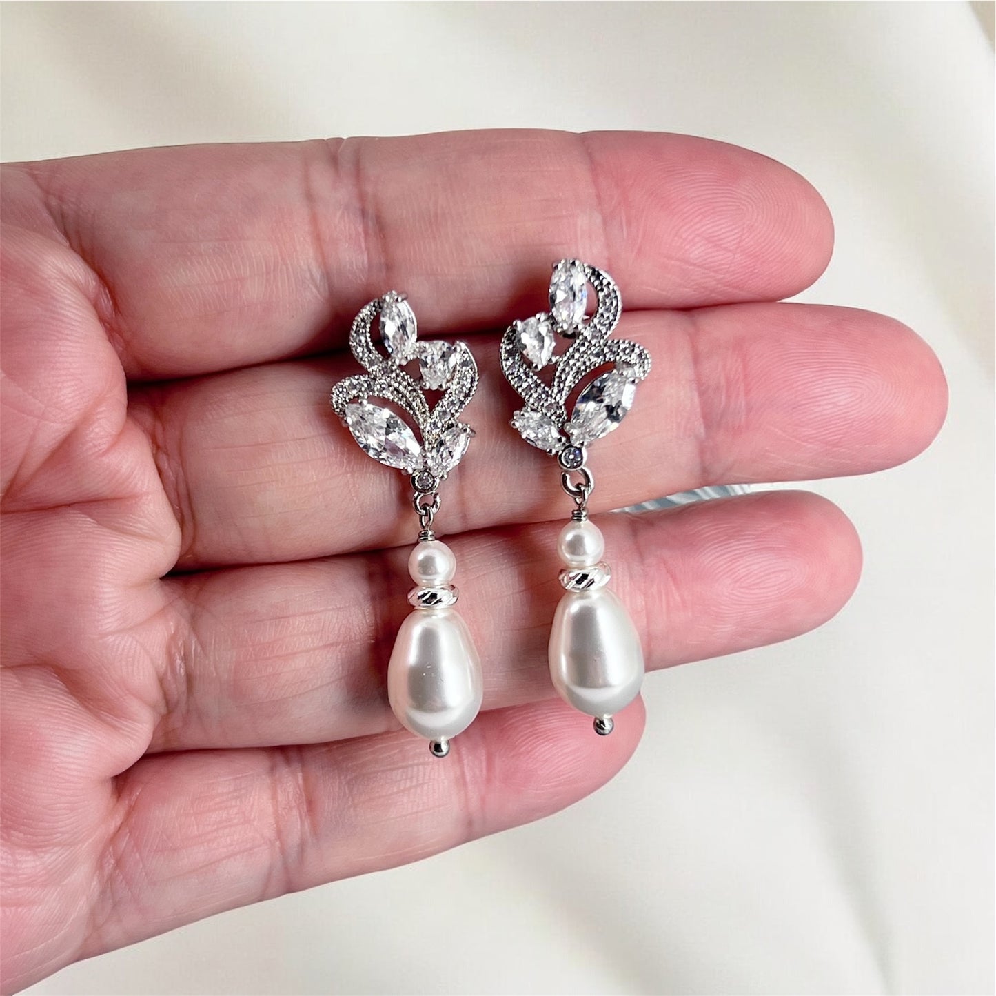 Silver floral earrings with pearls held in a hand against a white background