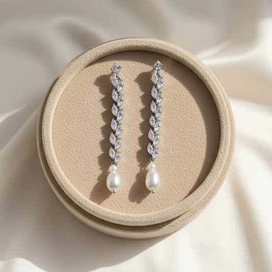Pair of silver earrings with leaf-like designs and pearl drops on a beige background